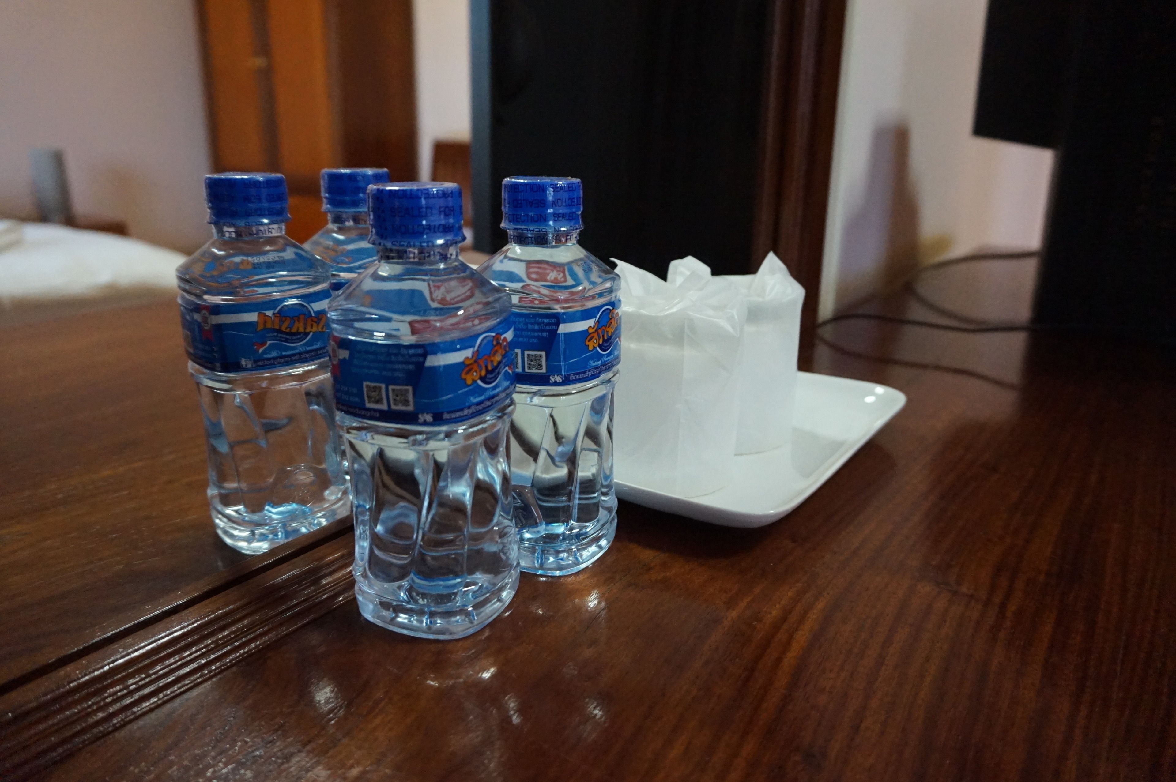 Cuatro botellas de agua cristalina sobre una mesa de madera con una bandeja blanca.