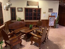 A traditional wooden dining area with a large table and chairs, a wall-mounted fan, and a bulletin board with various papers.