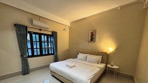 Une chambre d’hôtel avec un grand lit, une petite table de chevet, une fenêtre avec des rideaux, un appareil de climatisation et une lampe fixée au mur.