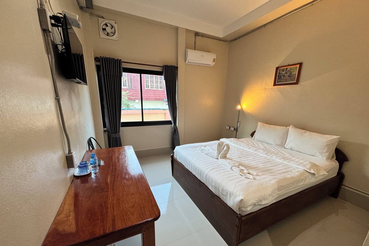 Quarto de hotel com escrivaninha de madeira, cama com toalhas bem organizadas, unidade de ar condicionado e janela com cortinas.