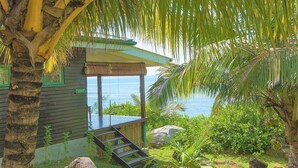 A tropical garden with a palm tree, a covered seating area, and a view of the sea. - South Point Villas (Cerf Island)