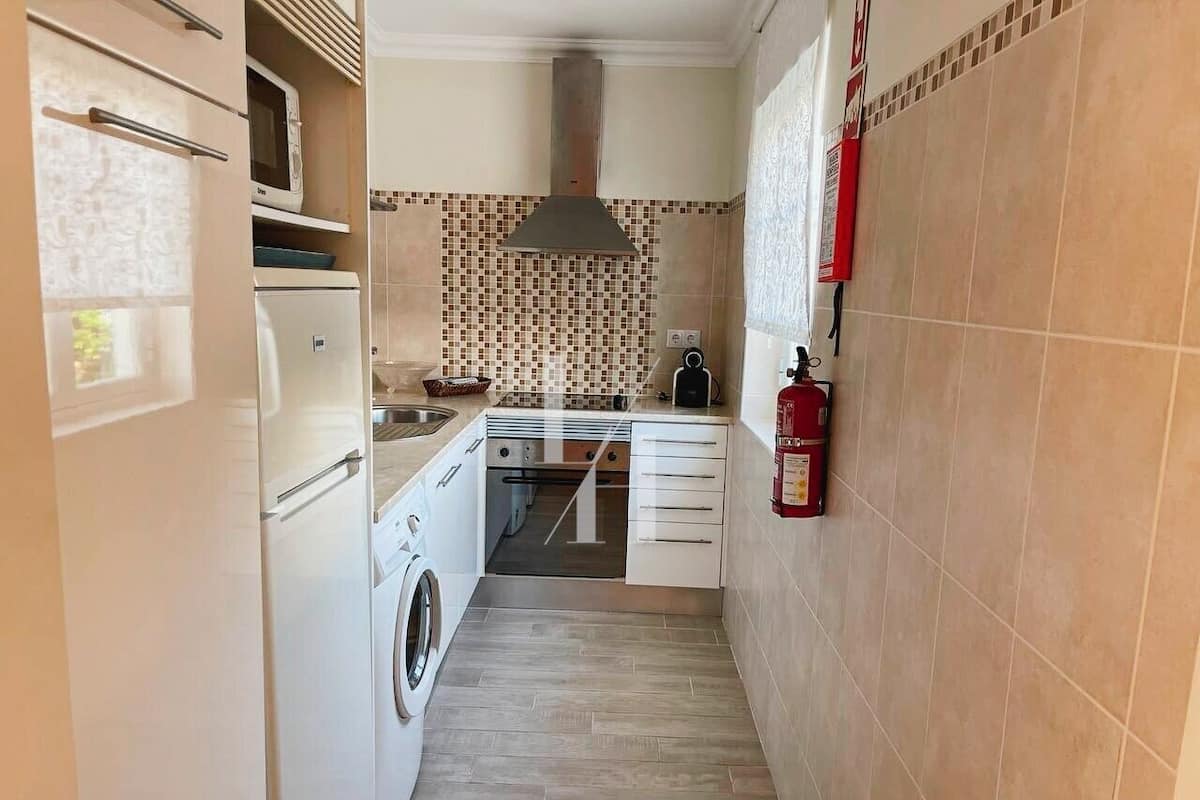 A narrow kitchen with a washing machine, a microwave, and a stove.