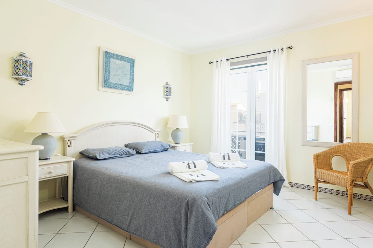 A bedroom with a bed, two bedside tables with lamps, a chair, and a window with curtains.