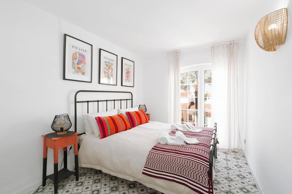 A neatly arranged bedroom with a bed, pillows, a bedside table, and wall art.