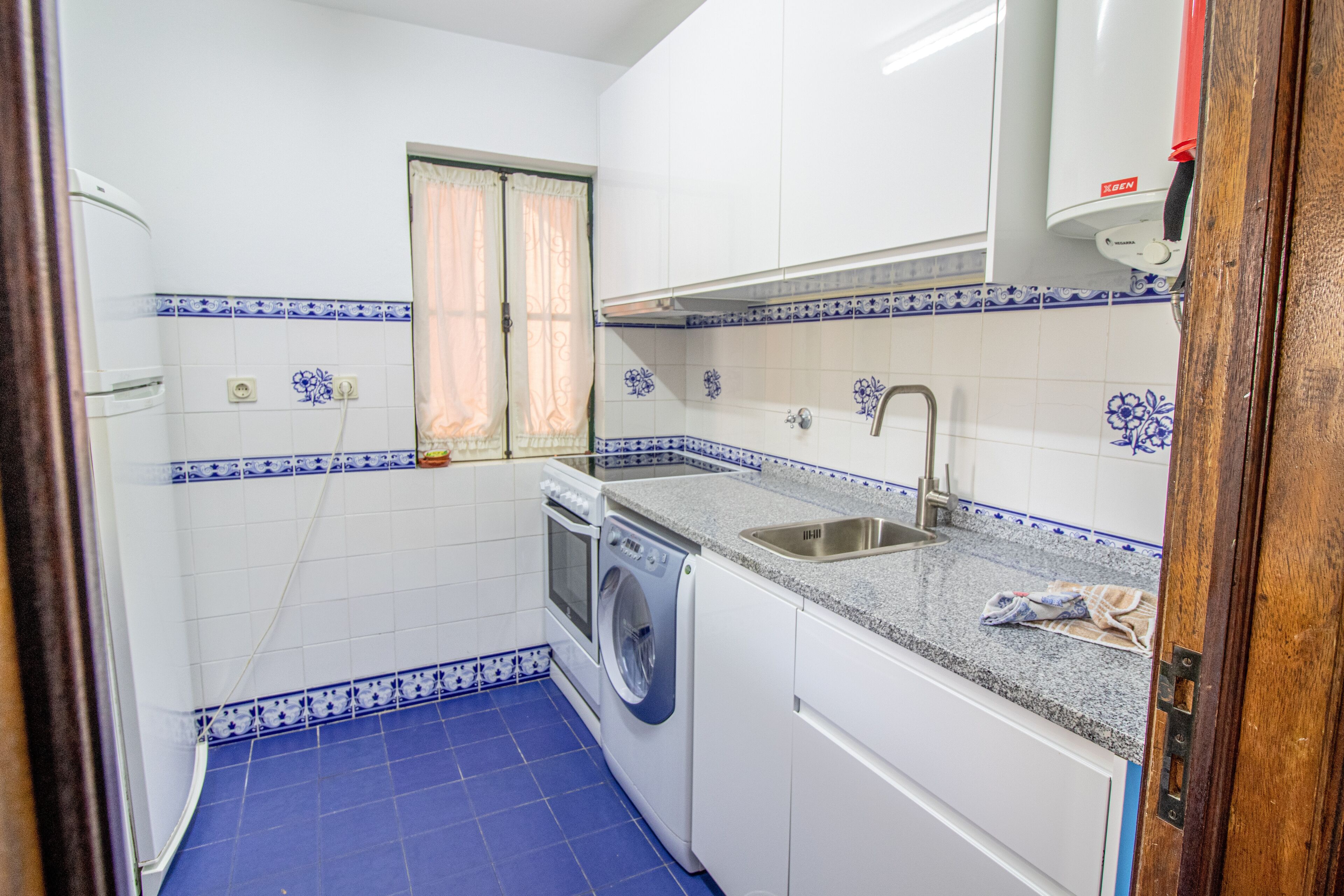 A compact kitchen with a washing machine, a sink, and a window with curtains.