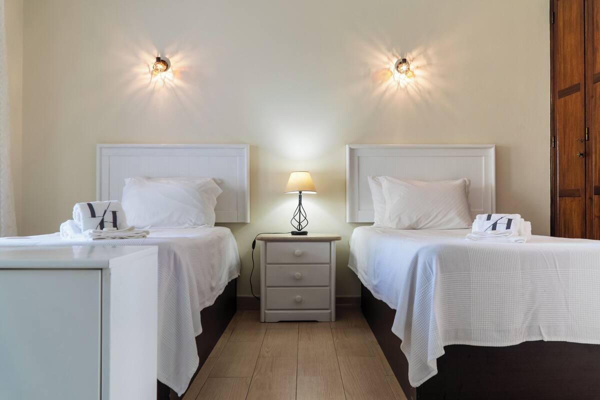 A hotel room with two beds, a nightstand with a lamp, and a wooden floor.