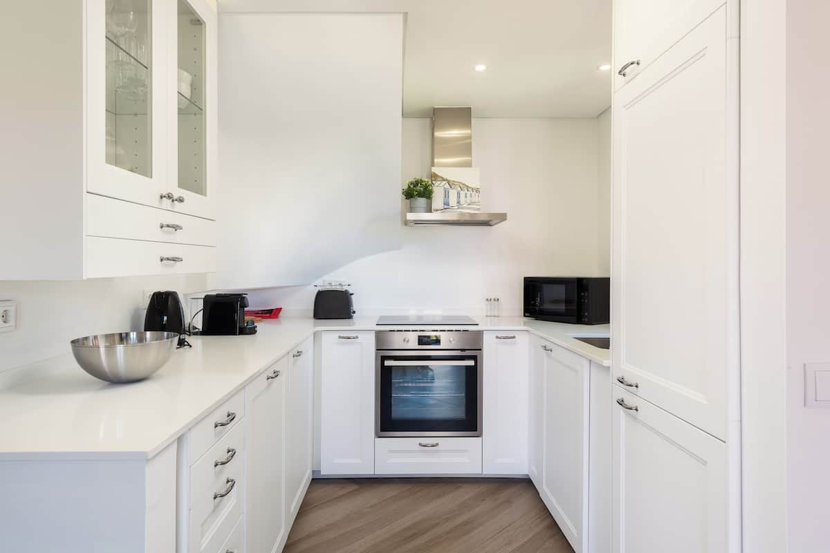 A modern kitchen with white cabinets, a stainless steel oven, and a microwave.
