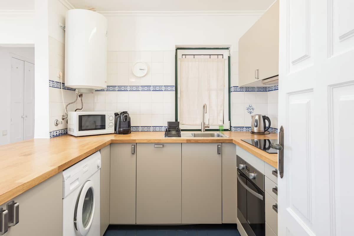 A compact kitchen with a washing machine, microwave, kettle, and a sink.