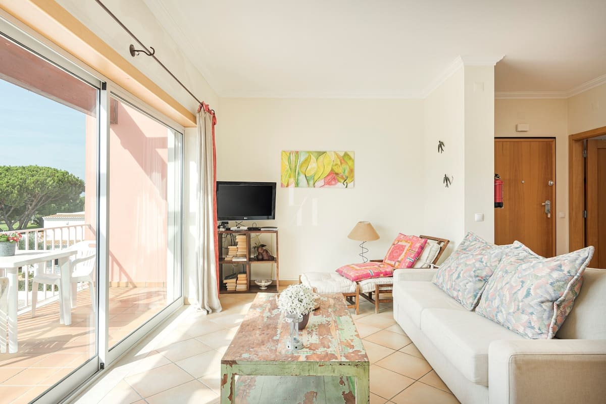 A living room with a sofa, a coffee table, a TV, and a balcony with a table and chairs.