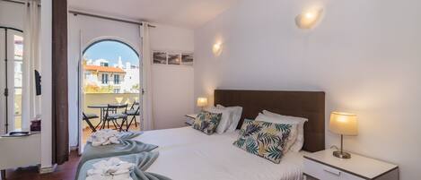 Une chambre d’hôtel avec un grand lit, une table de chevet, un bureau et une vue sur la ville, visible par une porte ouverte.