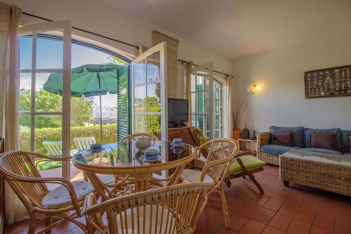 A cozy living area with wicker furniture, a television, and a view of the garden through large glass doors.
