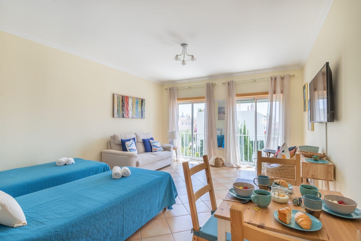 A room with two beds, a sofa, a dining table with breakfast items, and a TV on the wall.
