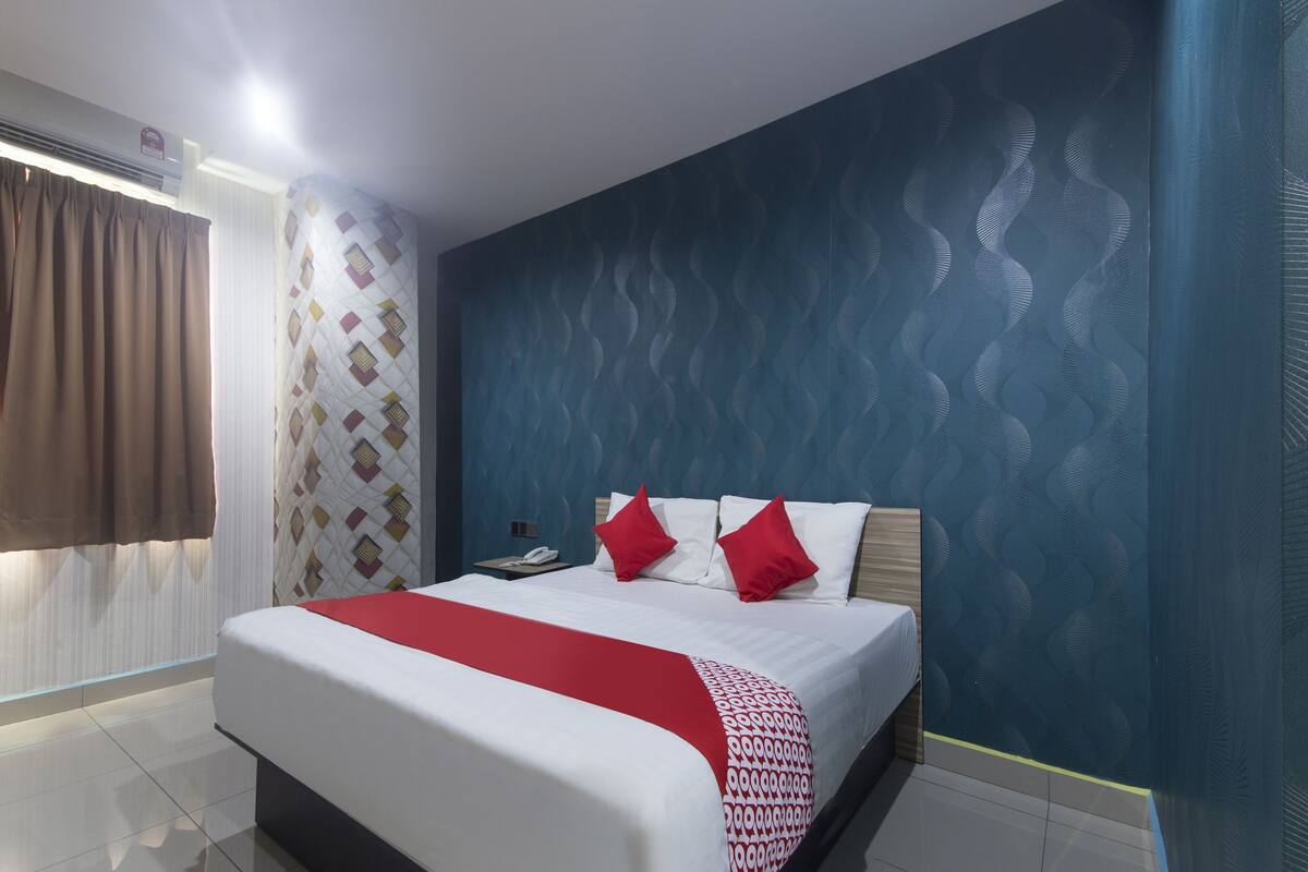 Quarto de hotel moderno com cama grande, mesa de cabeceira e parede com padrão.