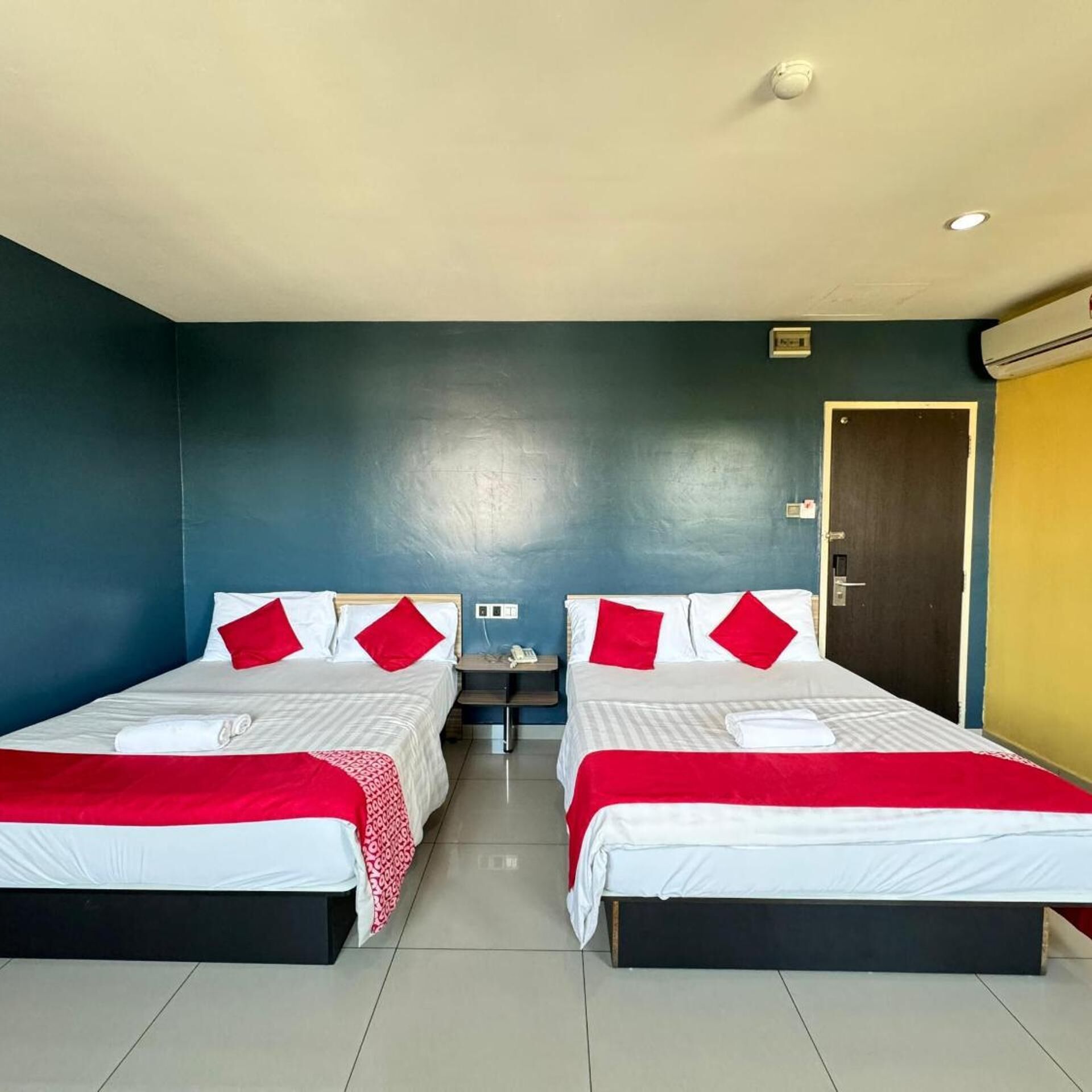 A hotel room with two beds, each with a red and white bedspread, a small bedside table, and a wall-mounted phone.