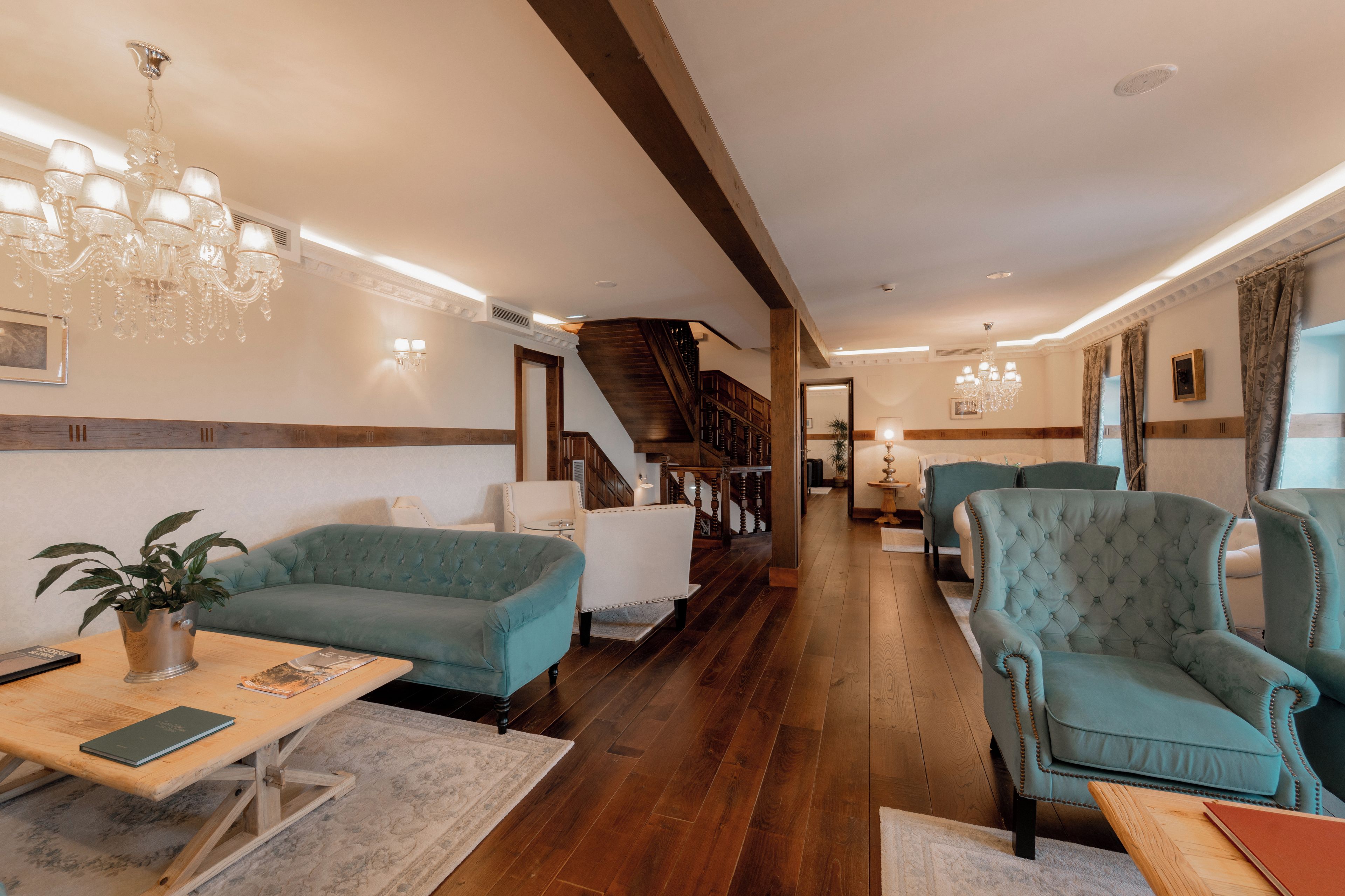 A spacious living area with a wooden staircase, a chandelier, and a view of the kitchen.