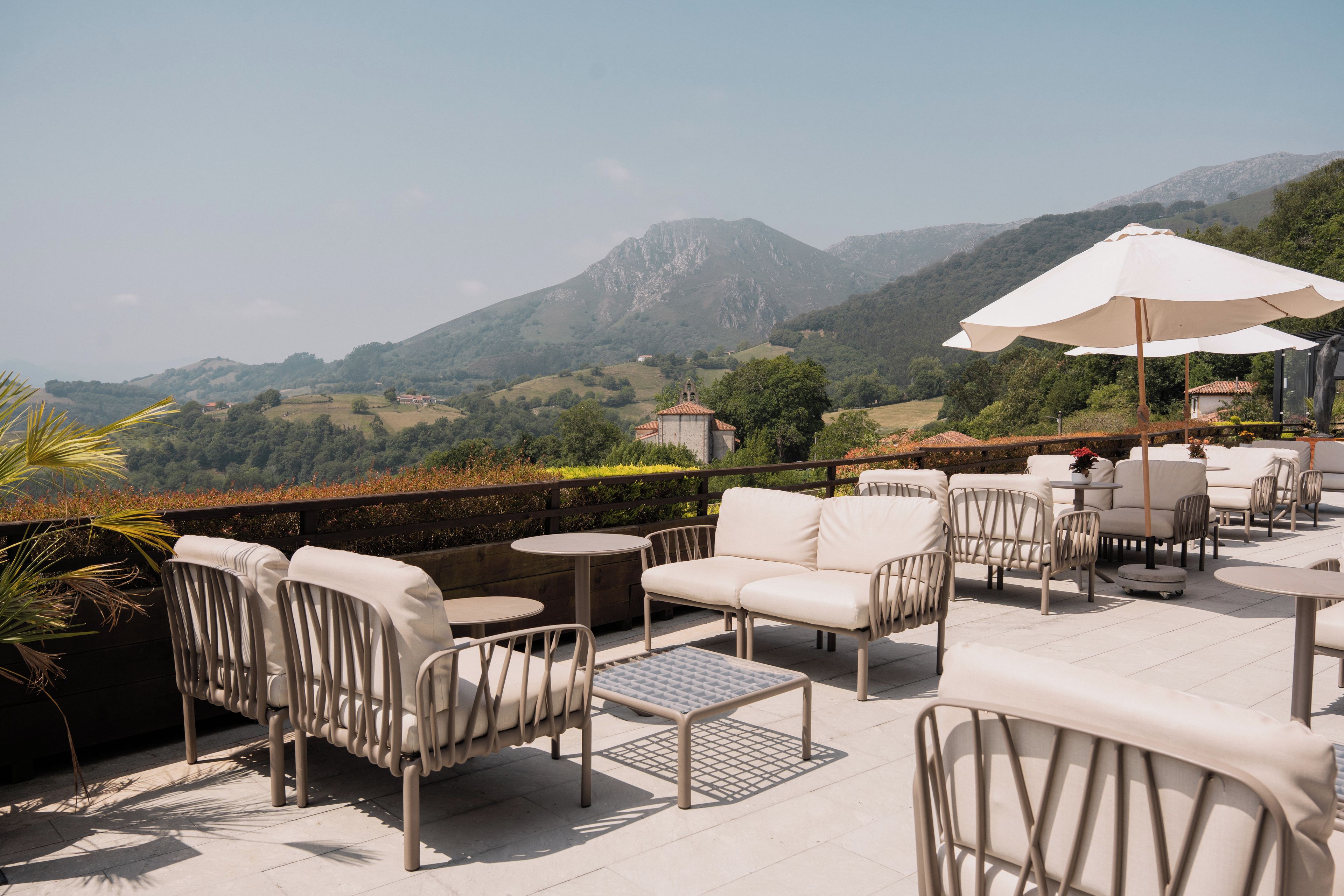 Una terraza con mobiliario exterior, una mesa y un gran paraguas, con vistas a un paisaje montañoso.
