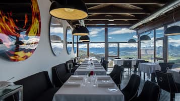 A restaurant with a long table set for dining, large windows with a mountain view, and modern pendant lighting.
