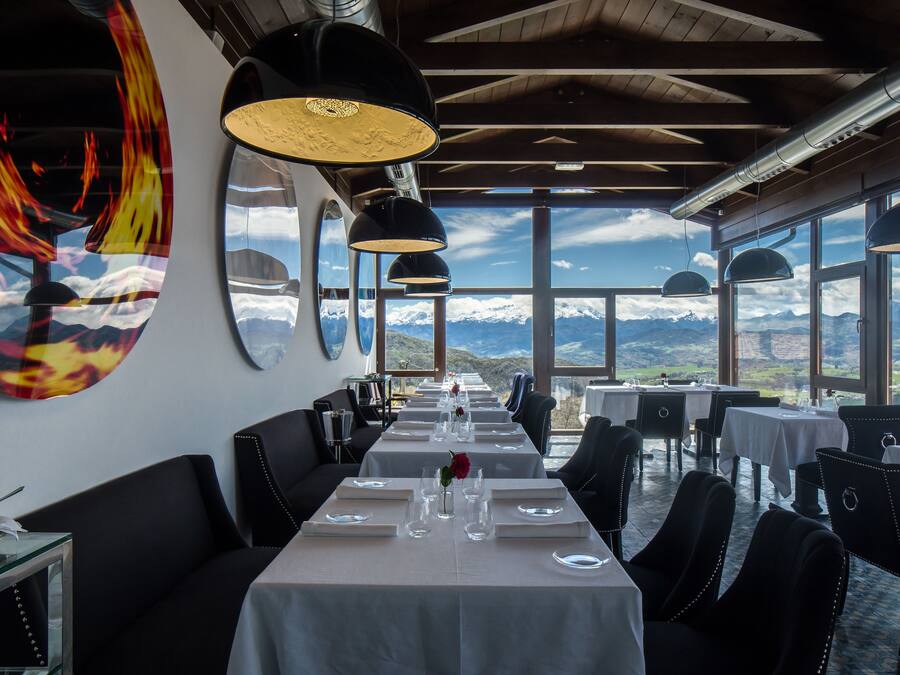 A restaurant with a long table set for dining, large windows with a mountain view, and modern pendant lighting.