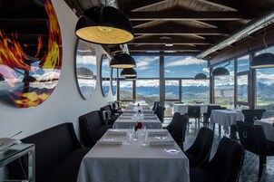 Un restaurante con una larga mesa dispuesta para comer, amplias ventanas con vistas a la montaña e iluminación colgante moderna.