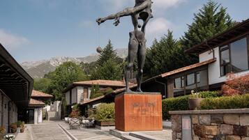 A sculpture of a figure holding a ball, with a mountain backdrop, in a courtyard with stone buildings and outdoor seating.