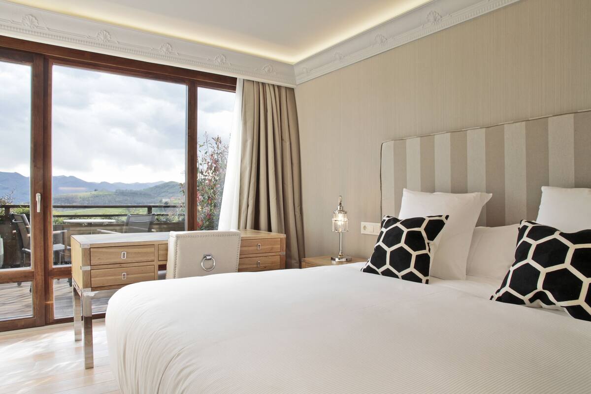Een hotelkamer met een groot bed, een bureau, een stoel, een nachtkastje en uitzicht op de omgeving.