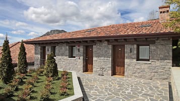 A stone building with a tiled roof, wooden doors, and a stone-paved courtyard.