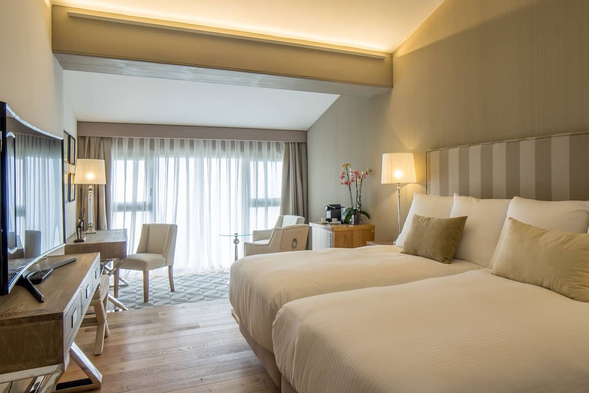 Een hotelkamer met een bed, een bureau, een stoel, een lamp en een raam met gordijnen.