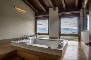 A modern bathroom with a large bathtub, wooden flooring, and large windows offering mountain views. - Puebloastur Eco-Resort Wellness & Spa (Parres)