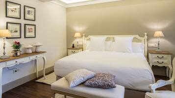 A neatly arranged hotel room with a large bed, bedside tables with lamps, a desk with a lamp and a vase of flowers, and framed pictures on the wall.