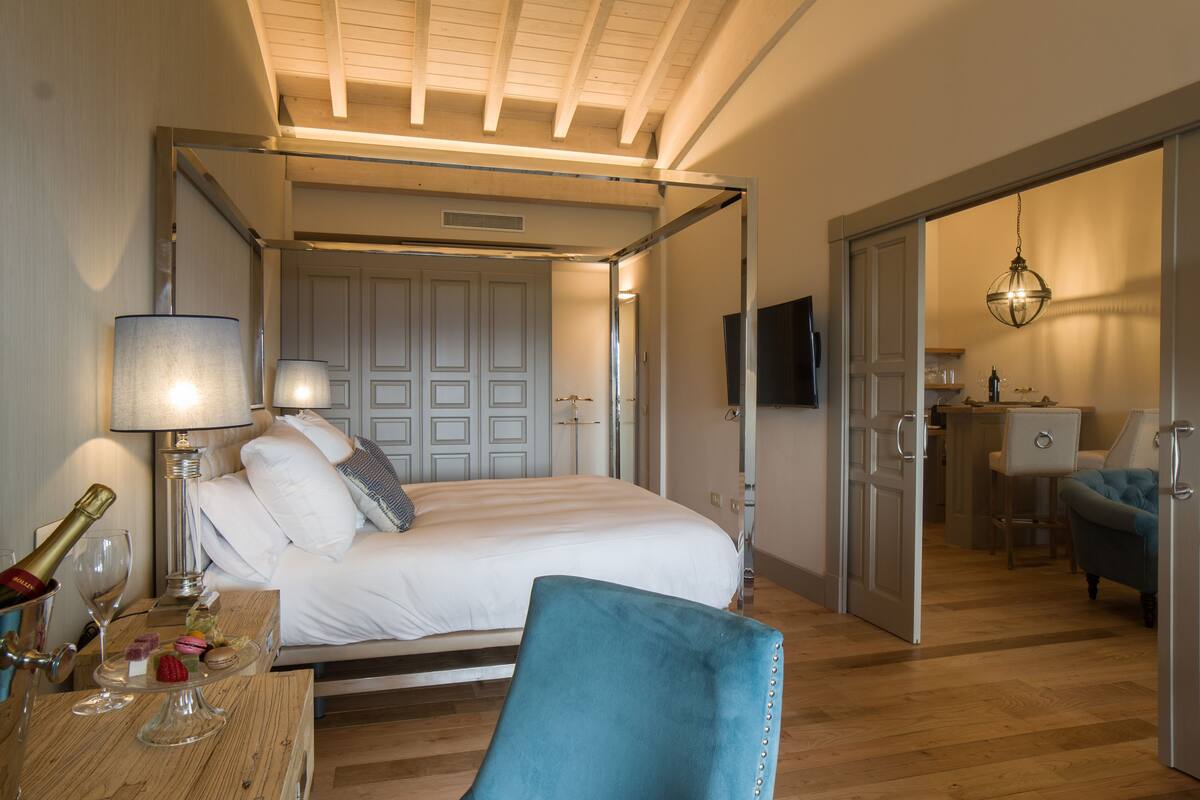 Een slaapkamer met een hemelbed, nachtkastje met lamp, champagnefles en een glas.