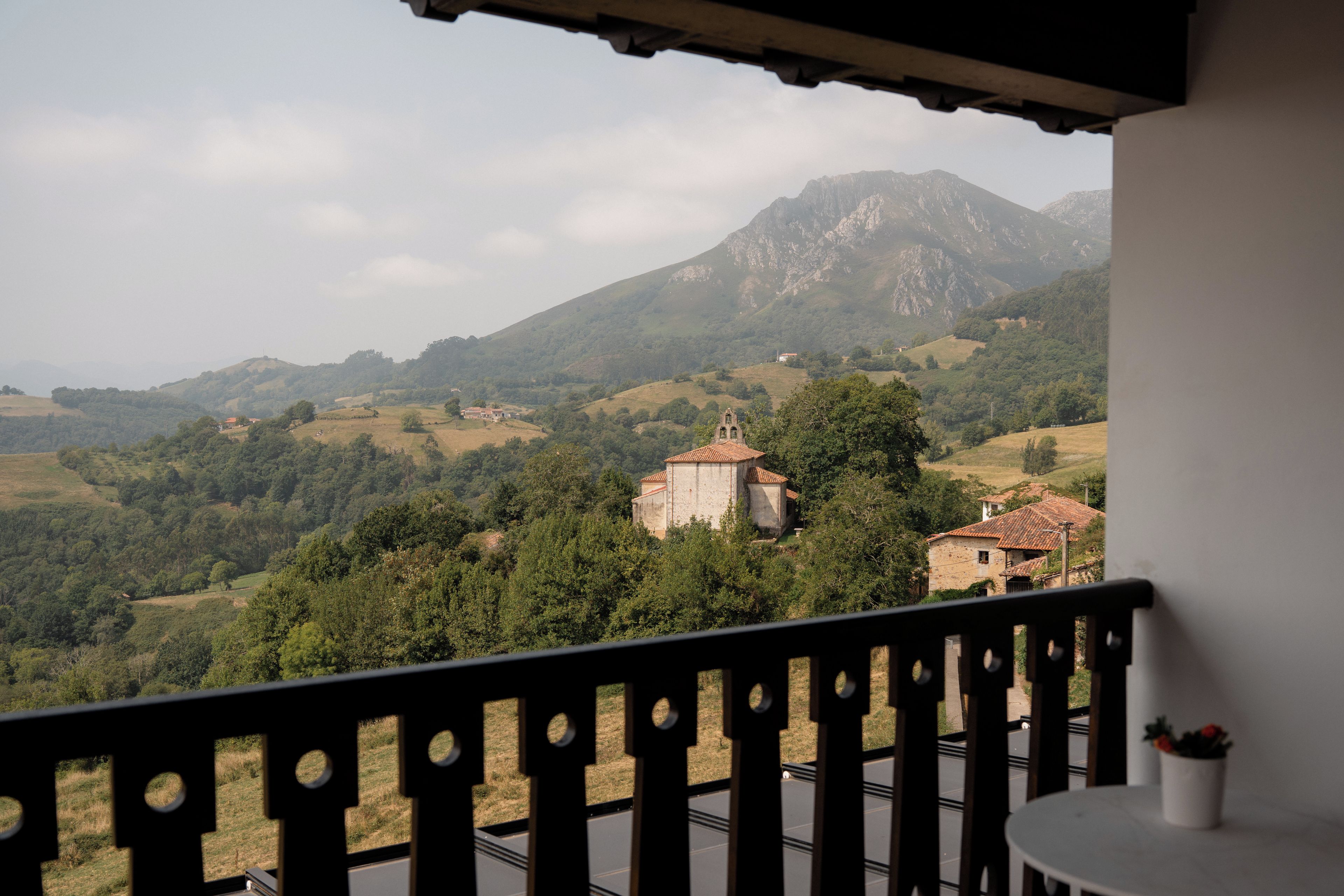 Een balkon met uitzicht op een bergachtig landschap, inclusief een kerk en woongebouwen.