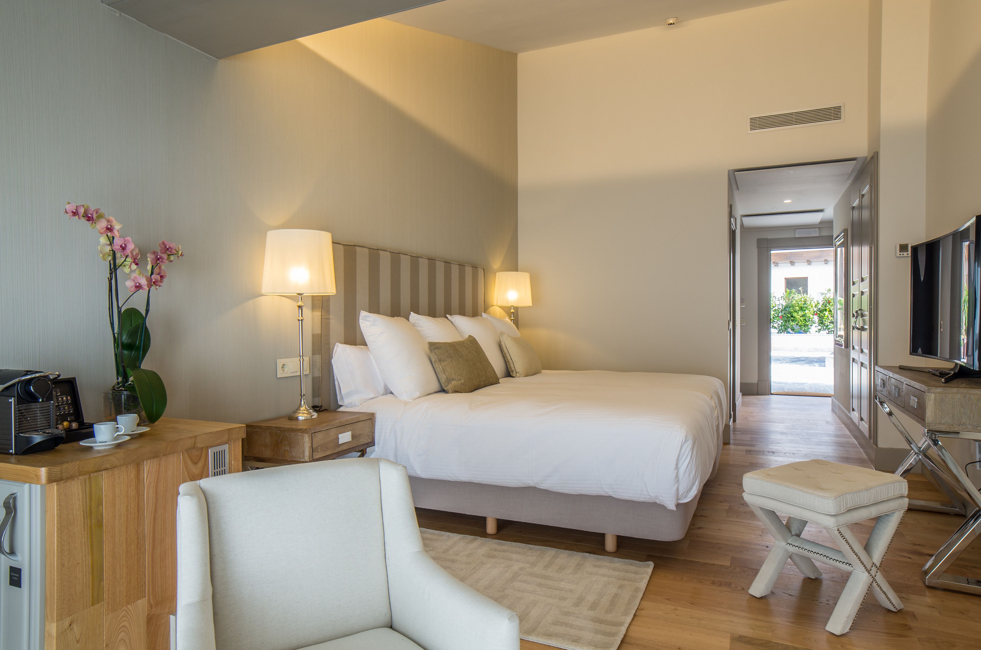 Una habitación de hotel moderna con una cama grande, lámparas de noche, un escritorio con cafetera y una televisión.