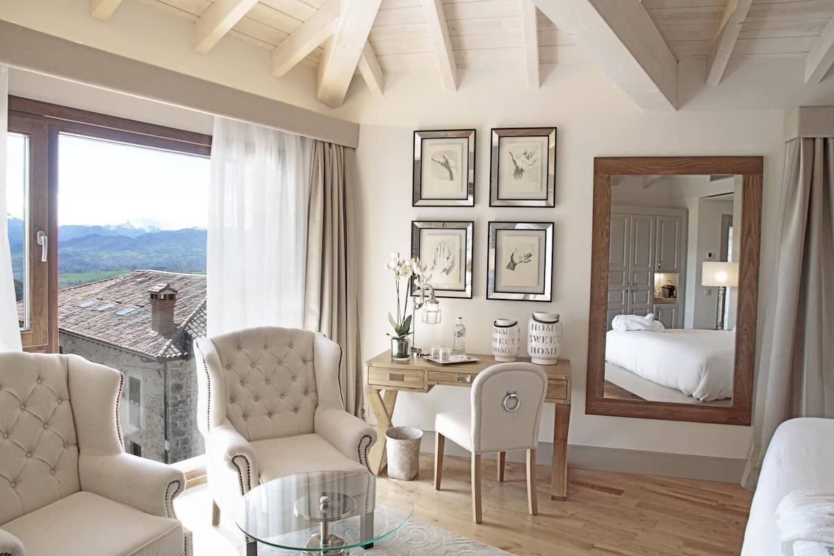 Een hotelkamer met een groot raam, een houten bureau, een zithoek en een bed.