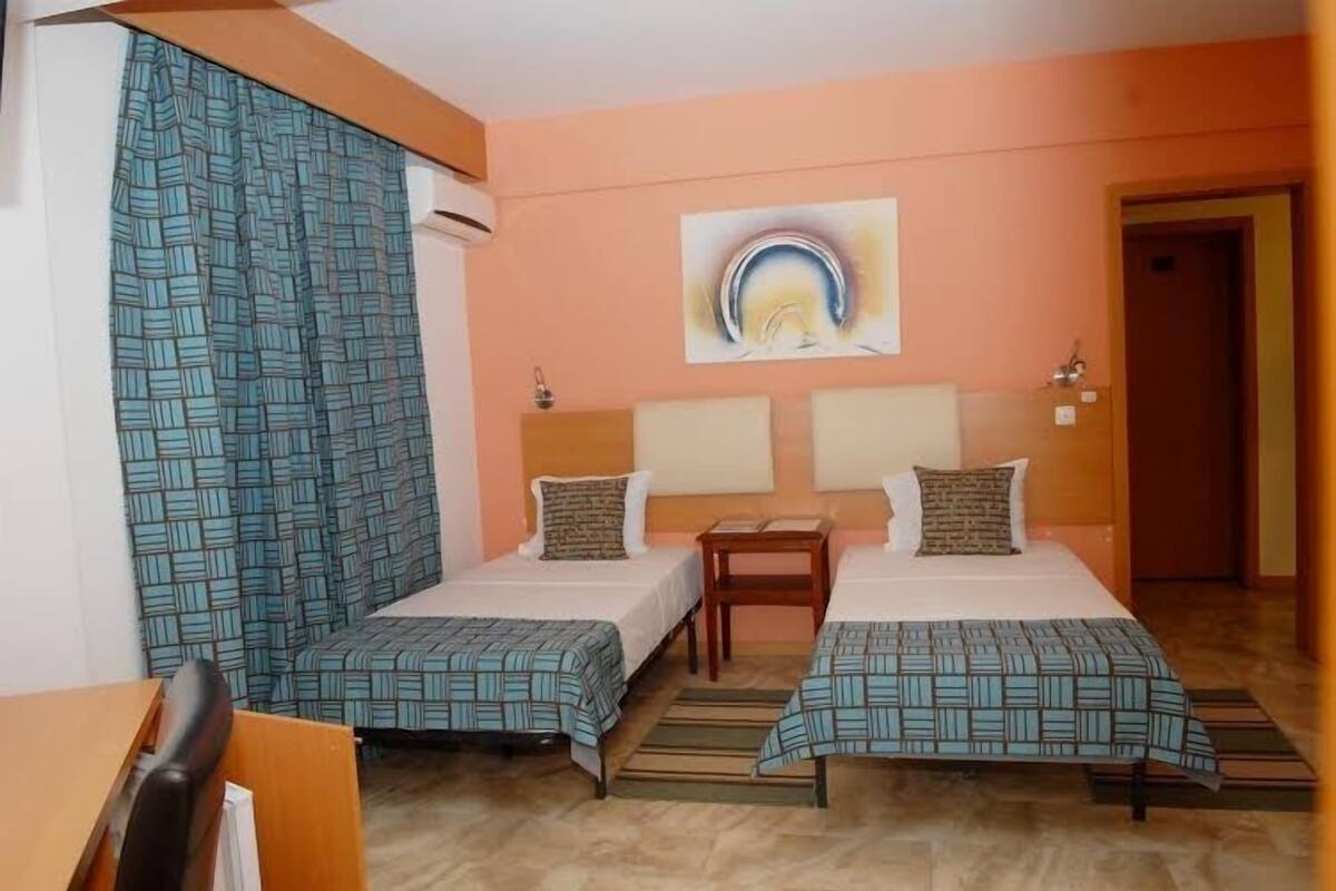 A hotel room with two beds, a wooden nightstand, a painting on the wall, and a patterned curtain.