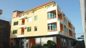 A multi-story building with a yellow facade, multiple balconies, and a ground-level entrance. - Miradouro de Gamboa (Praia)