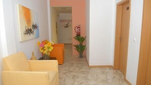 A hallway with a yellow sofa, a painting, a vase with flowers, and a door. - Miradouro de Gamboa (Praia)