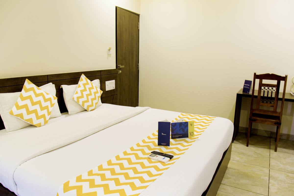 A neatly made bed with a chevron-patterned bedspread, a wooden headboard, and a wooden chair beside the bed.