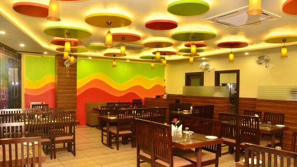 A restaurant with multiple dining tables and chairs, colorful ceiling lights, and a wavy wall design. - FabHotel Padmavati Palace Mansarovar (Jaipur)
