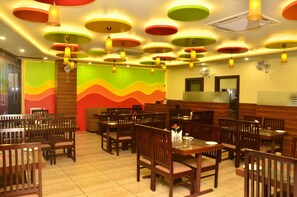 Un restaurante con varias mesas y sillas, luces de techo coloridas y un diseño de pared ondulado.