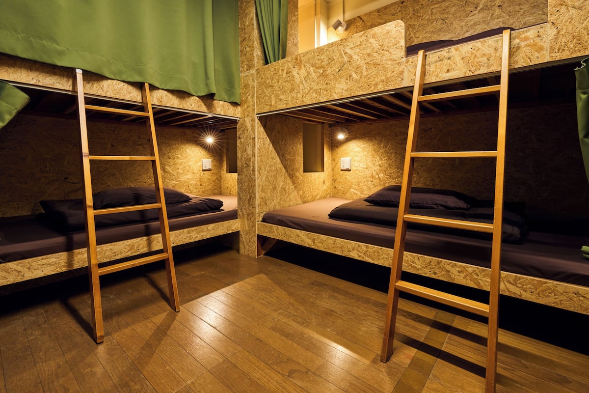 Een kamer met stapelbedden, houten vloeren en een groen gordijn.