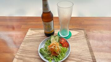 A bottle of Singha beer, a glass of water, and a plate of salad with cucumbers and tomatoes on a wooden table.