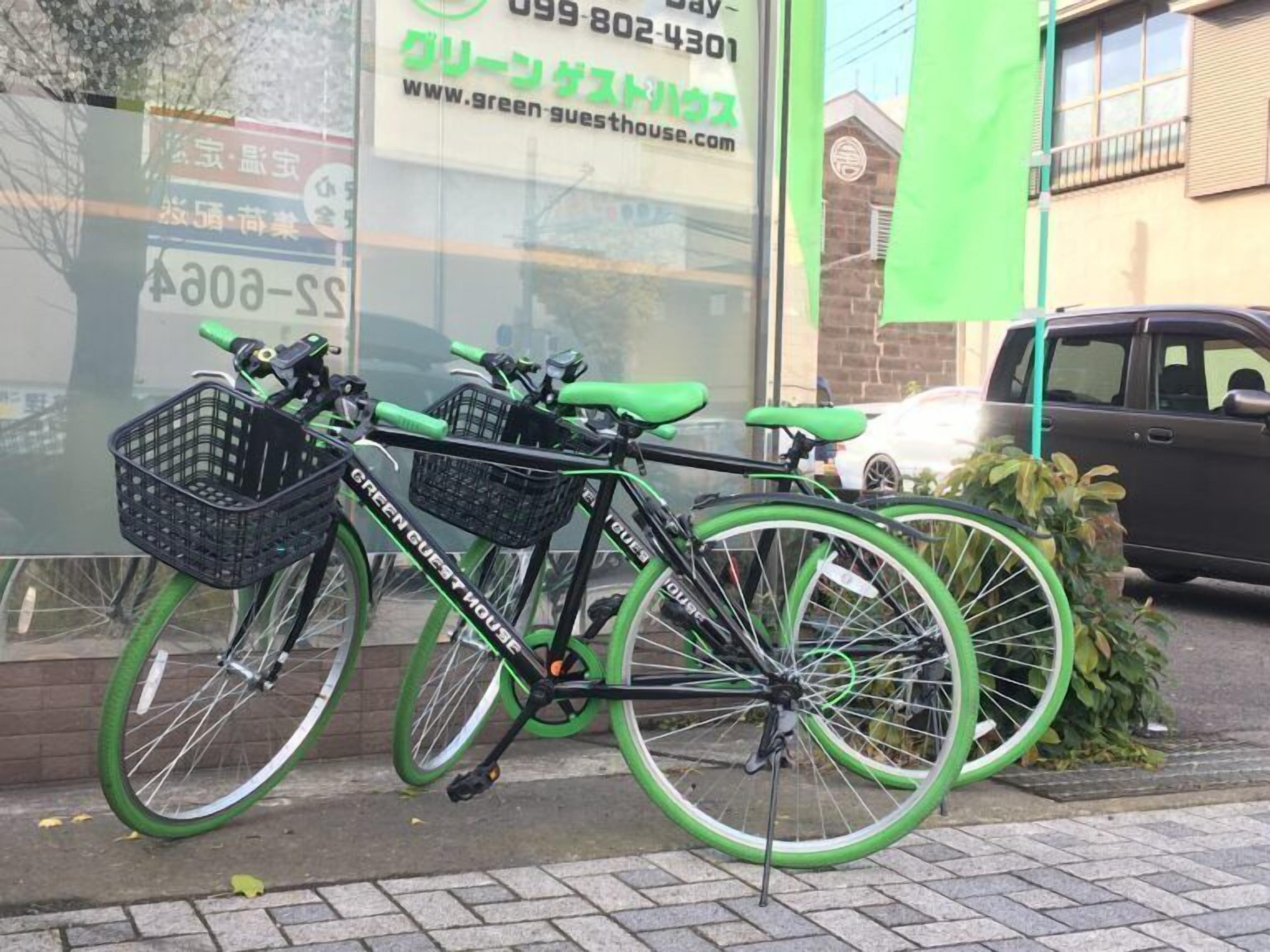 Una bicicleta con estructura verde y asiento negro, estacionada frente a un edificio que muestra una dirección web.
