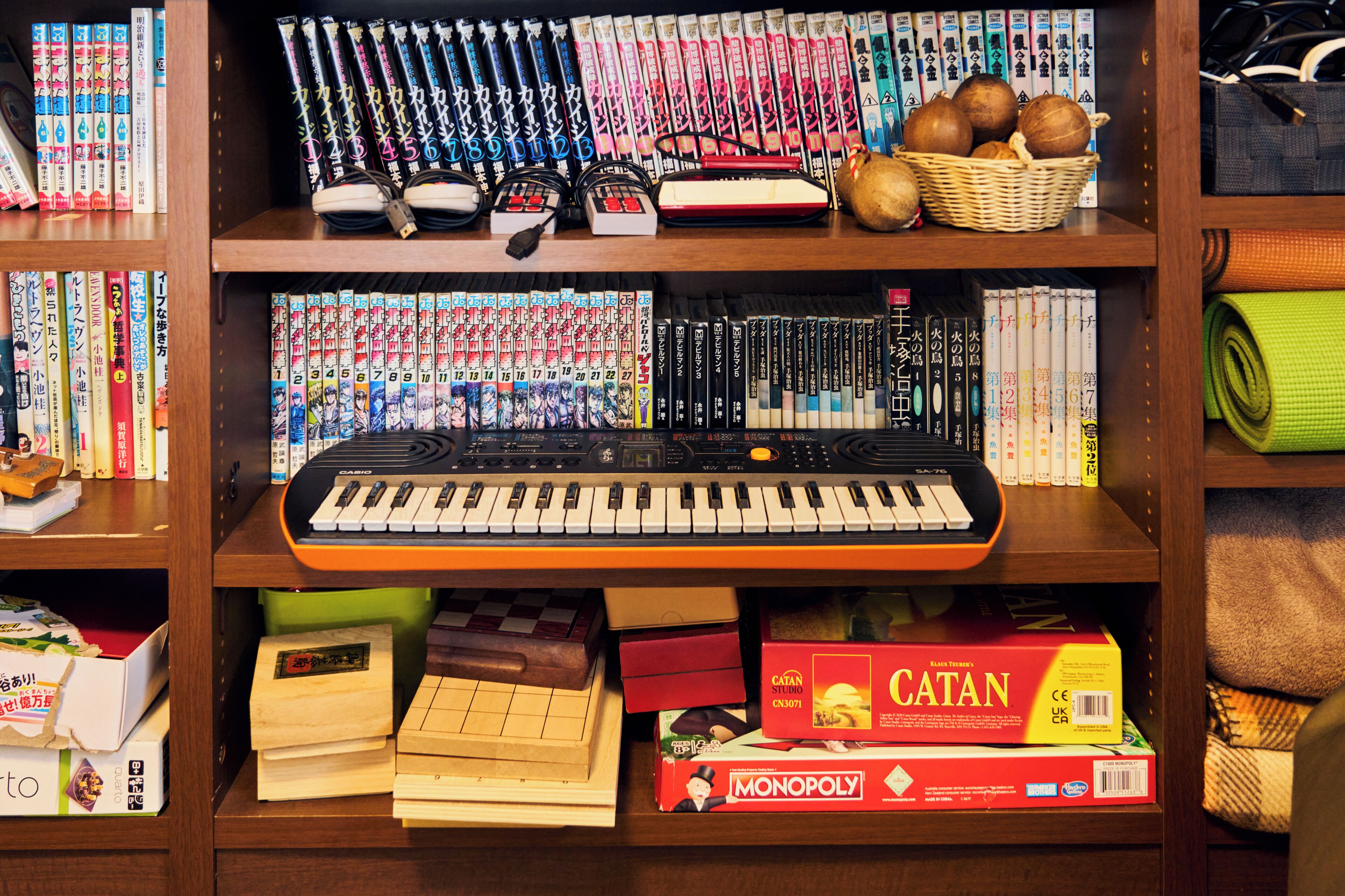 Una estantería con varios juegos de mesa, incluyendo Catan y Monopoly, y un teclado.