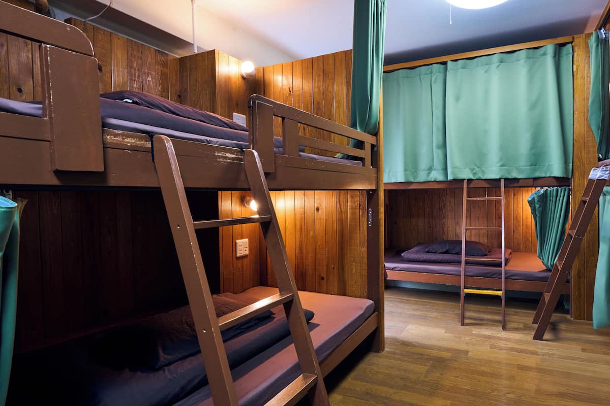Een slaapkamer met een stapelbed, houten wanden, een ladder en een groen gordijn.