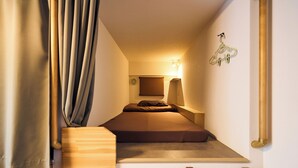 Ein kleines Zimmer mit einem Bett, einem Schreibtisch, einer Wandleuchte und einem Kleiderhaken.