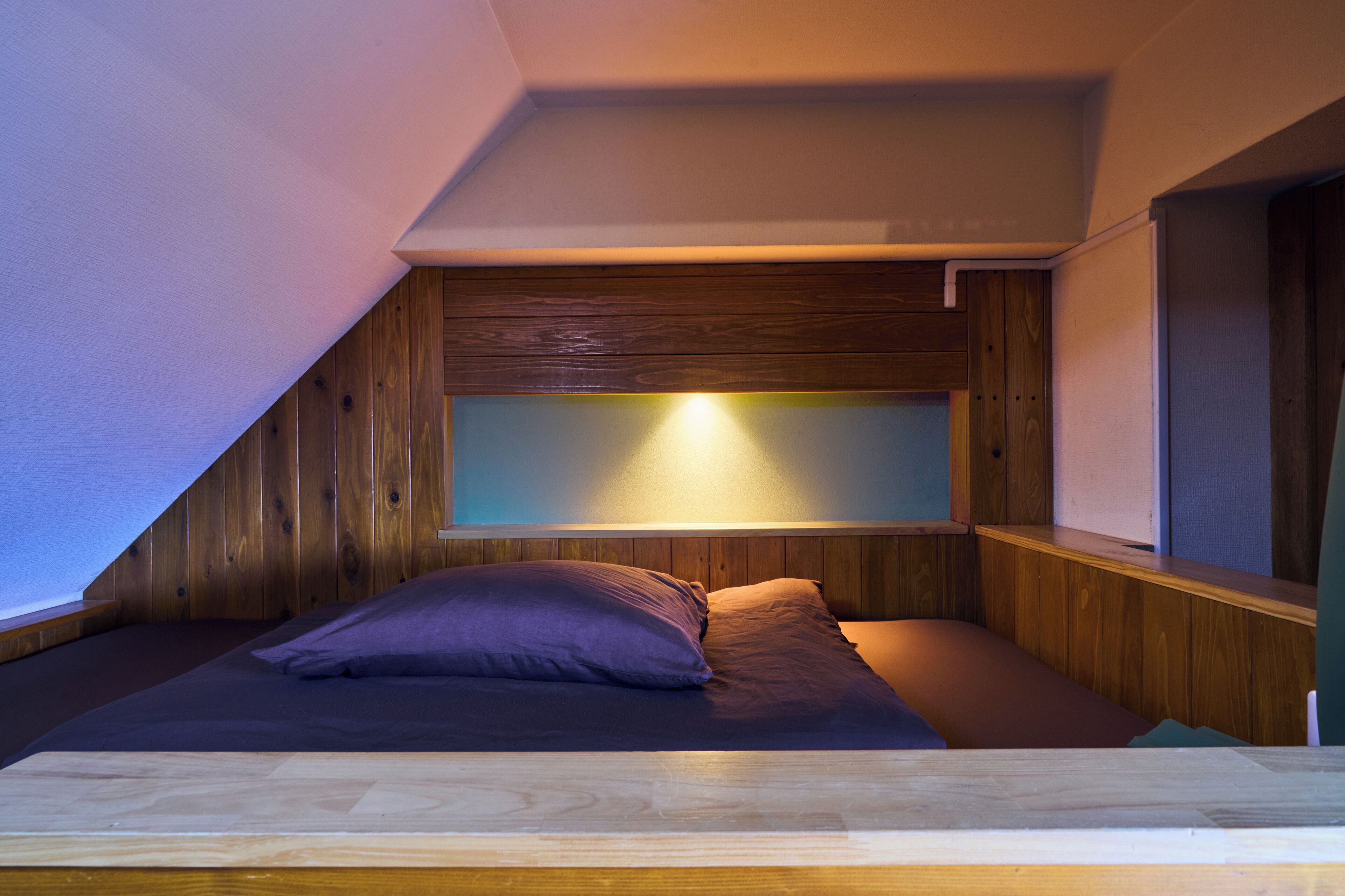 Una habitación pequeña y acogedora con techo inclinado, paredes de madera, una cama con almohadas y una mesita de noche.