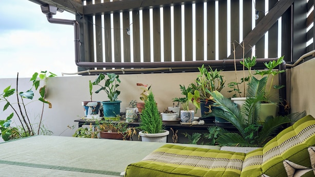 Ein Balkon mit einem Bett, grünen Kissen und verschiedenen Blumentöpfen.