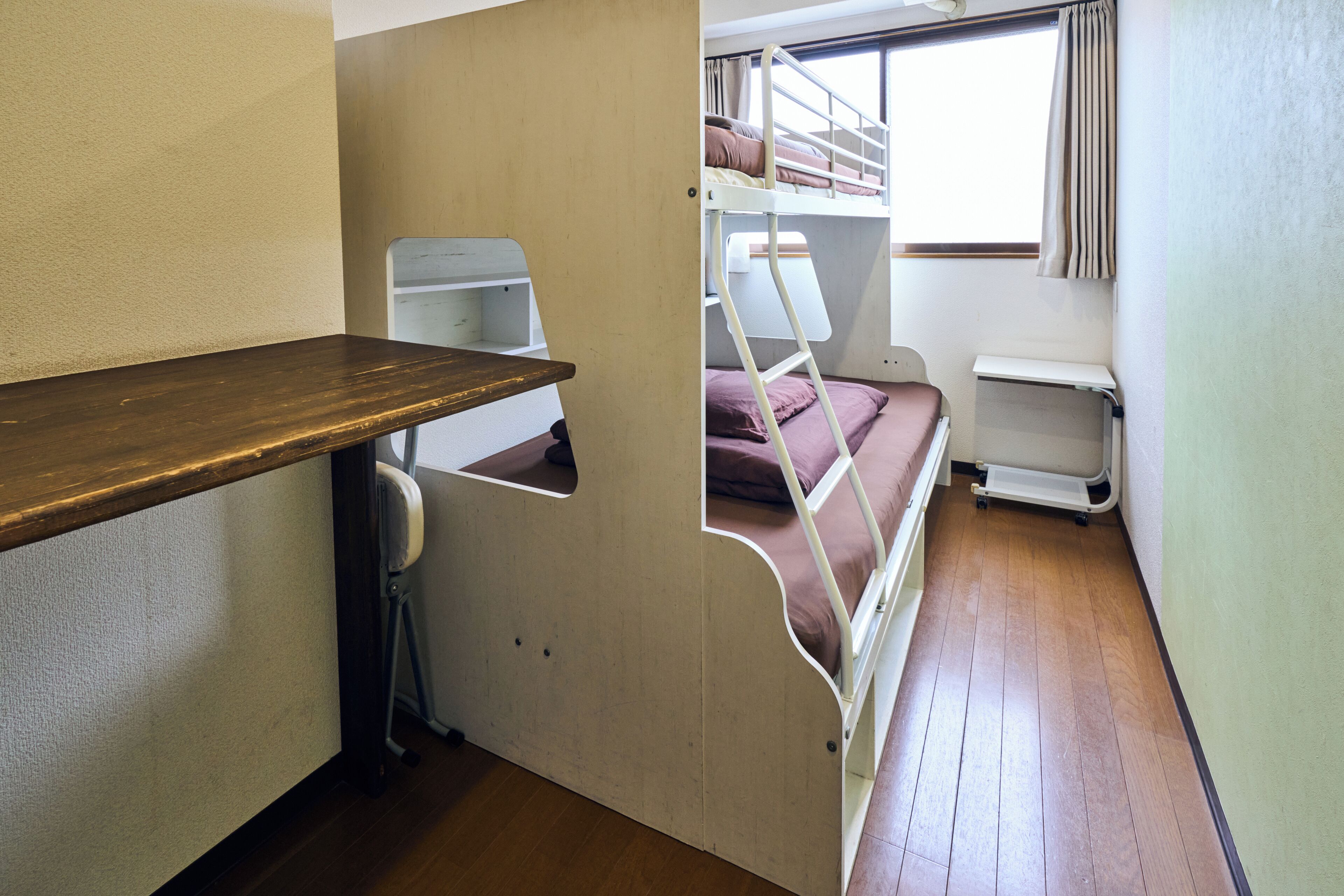 A bunk bed with a ladder, a small desk, and a window with curtains.