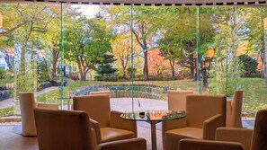 Un espace détente avec une table et des chaises en verre, donnant sur un jardin agrémenté d’arbres et d’un sentier.