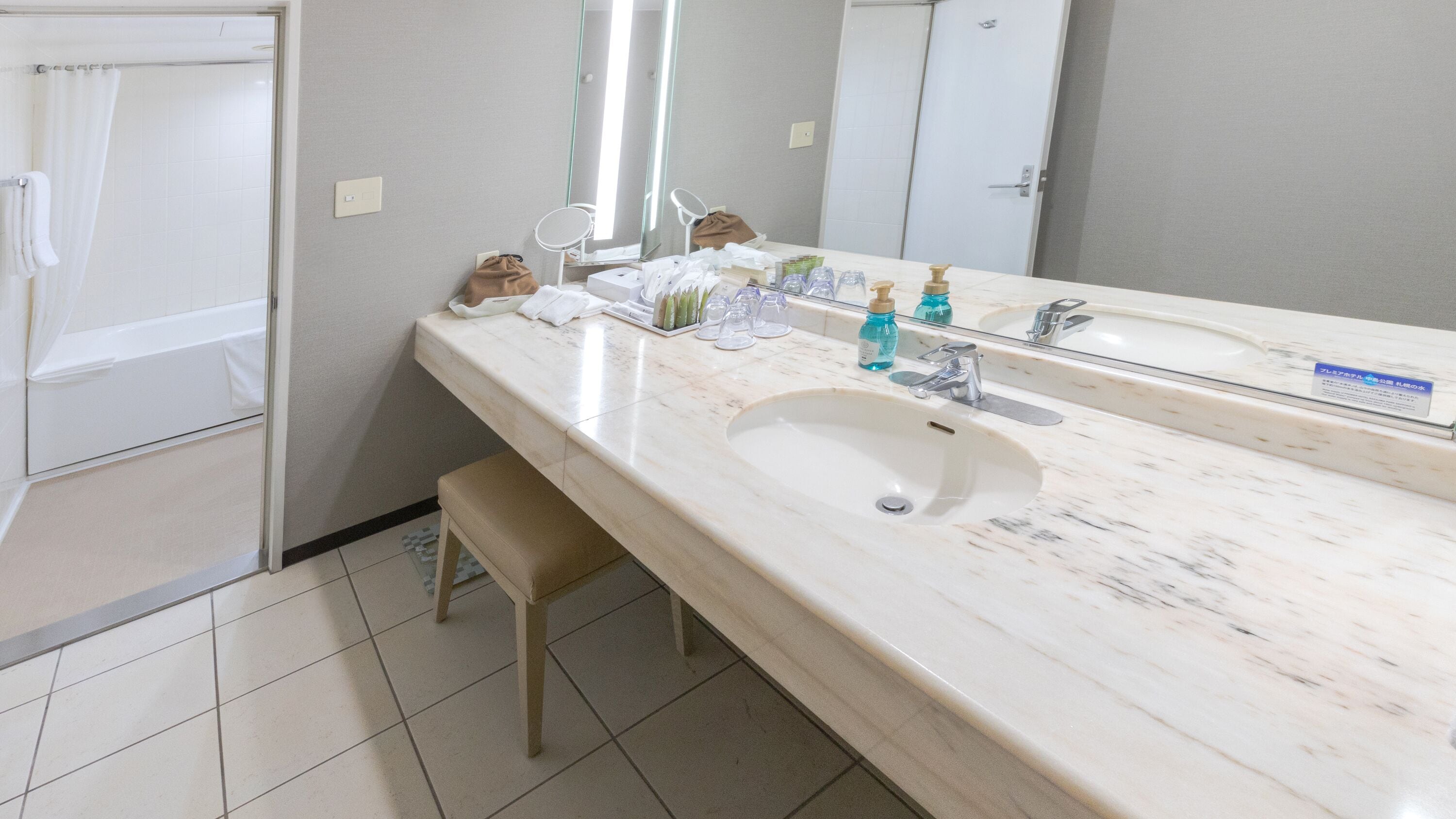 Ein Badezimmer mit Marmorwaschbecken, einem Spiegel, einem kleinen runden Tisch mit Toilettenartikeln und einer Duschvorhang.